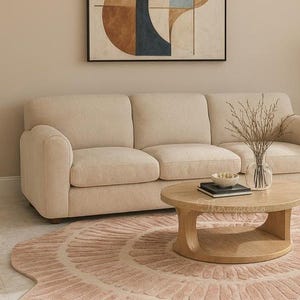 Pu&ograve; includere: Un divano beige con un tavolino rotondo in legno e un tappeto rosa. Il tappeto presenta un motivo circolare. Un vaso con rami secchi &egrave; appoggiato sul tavolo. Un dipinto astratto &egrave; appeso al muro.