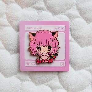 Puede incluir: Un pin de esmalte rosa y dorado con un personaje de anime chibi con cabello rosa, orejas de gato negras y un atuendo rosa y rojo. El personaje sostiene un animal chibi rosa y rojo. El pin está sobre un fondo rosa con un borde blanco y el texto "CHIBI HUGS!" en la parte superior.