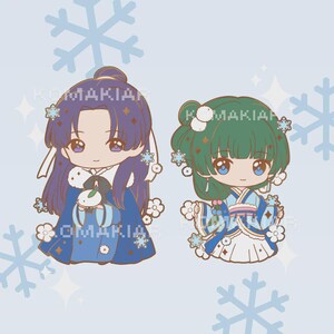 May include: Two chibi figures in winter outfits. One has purple hair and a blue outfit, the other has green hair and a blue and white outfit. Both figures have snowflake and flower accents. The text "KOMAKIAN" is visible.