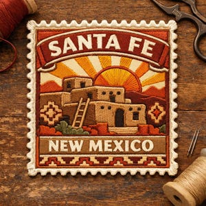 May include: Embroidered patch in a postage stamp design featuring "SANTA FE NEW MEXICO". The patch depicts a Southwestern landscape with adobe buildings, a rising sun, and decorative elements in shades of brown, orange, and cream.