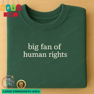 Peut inclure: Un sweat-shirt vert foncé avec le texte brodé "big fan of human rights" en blanc. Le sweat-shirt a un col rond et des manches longues. L'image comprend également un logo et le texte "LARGE EMBROIDERY AREA".