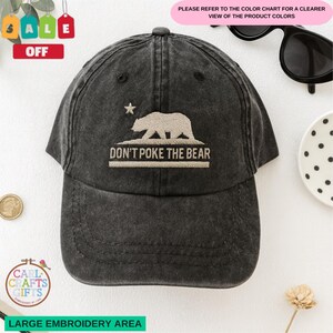 May include: A black baseball cap with the embroidered phrase "DON'T POKE THE BEAR" and a bear graphic. The cap also features a star and is made of a distressed fabric. The cap has a curved brim and an adjustable strap.