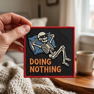 May include: Square black patch with a red border featuring a cartoon skeleton wearing sunglasses, relaxing on a blue pillow. The words "DOING NOTHING" are in orange block letters below the skeleton.