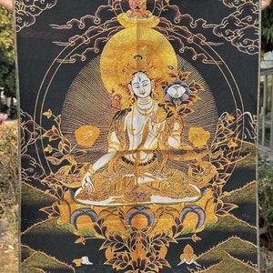 May include: A detailed tapestry featuring a seated deity with a golden halo and intricate gold embroidery. The background is black with gold accents, including clouds and mountain motifs. The deity holds a lotus flower.