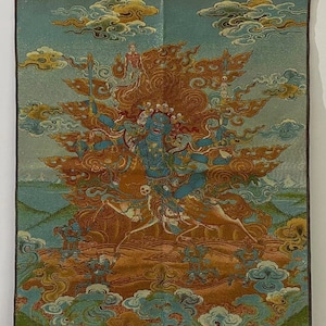 Puede incluir: Un tapiz detallado que representa una deidad azul con múltiples brazos, rodeada de llamas y nubes. La obra de arte presenta un fondo celestial con una cordillera en la parte inferior. La paleta de colores incluye azules, naranjas y oro.