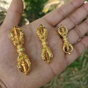 May include: Three gold-coloured Vajra scepters of varying sizes are displayed. The scepters have intricate floral and geometric designs. The smallest scepter is approximately 5 cm in length, while the largest is about 10 cm long.