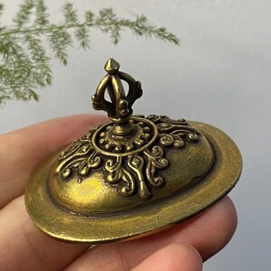 May include: A detailed, antique-style brass lid with an ornate design. The lid features a central crown-like handle and intricate floral patterns around the edge. The brass has a warm, aged patina, suggesting it is vintage or vintage-inspired.