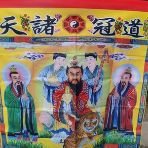 May include: A yellow banner with Chinese characters and illustrations of figures in traditional attire. The banner features a central figure with a stern expression, surrounded by other figures and a tiger. The top is red.