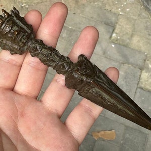 May include: An antique bronze dagger with an elaborate handle, showing a sculpted face and detailed patterns. The blade is long and pointed. The design suggests a ceremonial or decorative item, possibly of historical significance.