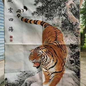 May include: A decorative tapestry featuring a detailed illustration of a tiger with orange and black stripes, set against a backdrop of a snowy landscape and a pine tree. The tapestry has Chinese characters on the left side.
