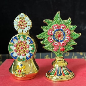 May include: Two decorative gold ornaments. One is a rounded shape with a floral design in white, blue, pink, and red. The other is a stylized flower with green leaves and a similar floral pattern. Both have intricate details and are highly decorative.