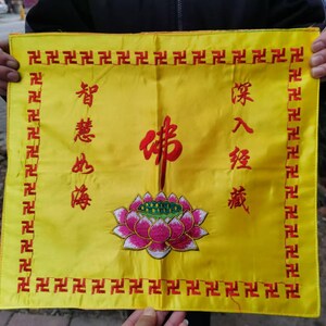 May include: Yellow rectangular banner with red text and symbols. The banner features a lotus flower and Chinese characters. The border is adorned with a repeating pattern of red symbols. The banner is held by a person.