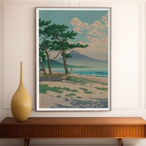 May include: A vintage Japanese woodblock print depicting a mountain range, a body of water, a boat on the shore, and two pine trees. The print is framed in a white frame.