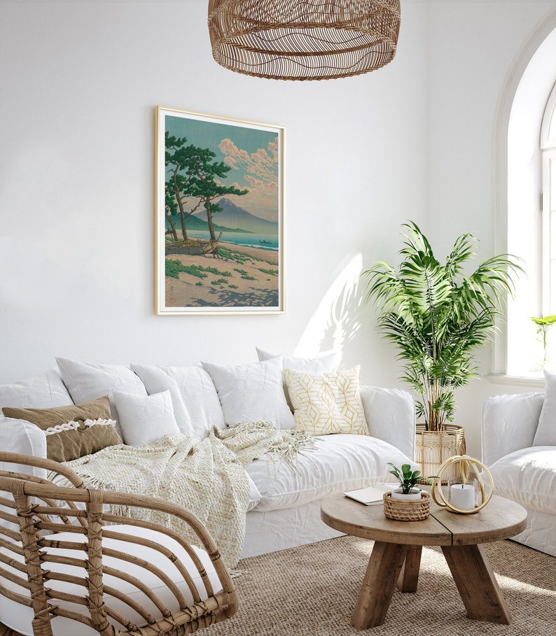 May include: A white couch with pillows and a throw blanket sits in a living room with a wooden coffee table and a potted plant. A framed print of a Japanese landscape hangs on the wall above the couch.