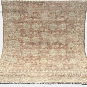 May include: A rectangular, vintage-style rug with a faded, distressed appearance. The rug features a warm, reddish-brown background with a repeating pattern of large, circular motifs in a lighter beige color. The edges have a fringed border.