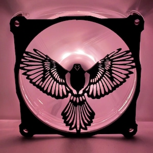 Può includere: Una griglia di ventilatore in metallo nero con un design ritagliato di un uccello in volo. La griglia del ventilatore è illuminata da dietro con una luce rosa.