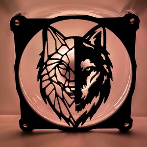 May include: A black metal fan grill with a cutout design of two wolf heads facing each other. The wolf heads are stylized and have a geometric pattern.