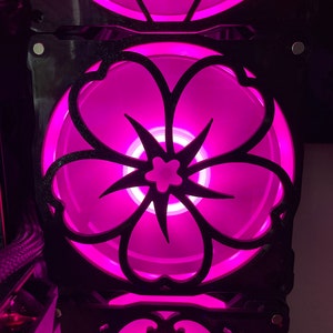 May include: A black computer case with a pink, flower-shaped fan. The fan has a black, intricate design and is illuminated with pink light.