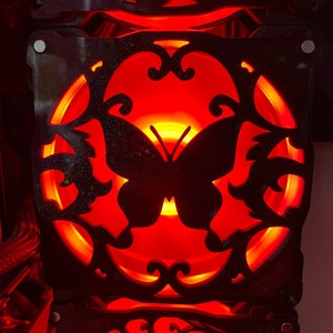 May include: A black metal fan grill with a red light shining through the intricate butterfly design.