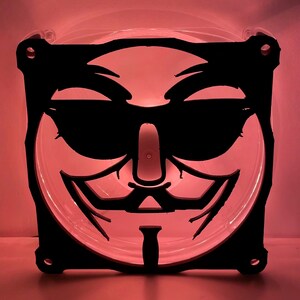 May include: A black and white computer fan with a stylized image of a person wearing a mask. The mask has a sharp, angular design and a prominent nose.
