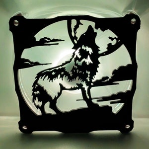 May include: A black silhouette of a wolf howling at the moon, cut out of a clear plastic fan. The wolf is facing the right side of the image and is howling with its mouth open. The moon is behind the wolf and is partially obscured by the wolf's head.