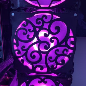 May include: Three black computer case fans with intricate cut-out designs. The fans are illuminated with a bright purple light.