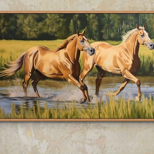 May include: Two golden horses run through a shallow stream of water. The horses are in a field with green grass and trees in the background.