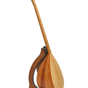 Può includere: Uno strumento a corde in legno, probabilmente un saz o uno strumento popolare simile, appoggiato su un supporto in legno marrone scuro. Lo strumento ha un corpo a forma di pera e un lungo manico con piroli.