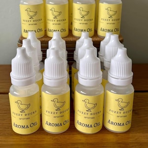 May include: A collection of small, clear glass bottles with white dropper tops. Each bottle has a yellow label with a cartoon duck and the text "Fuzzy Ducks Aromas Aroma Oil".