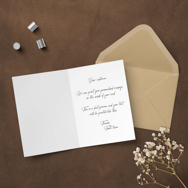 The inside of a custom greeting card showing a preview of a personalized printed message, laid out on a rustic brown surface next to a premium kraft envelope and dried floral decor.