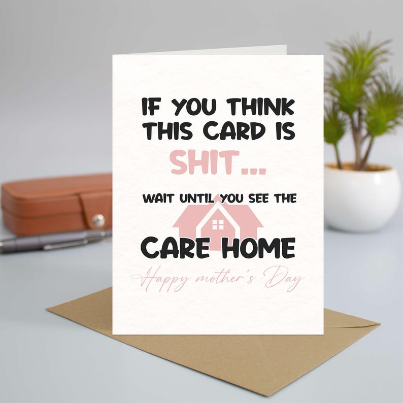 A hilarious Mother's Day greeting card reading "If you think this card is shit wait until you see the care home," propped up on a desk against a kraft envelope, next to a pen and a small houseplant.