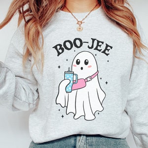 May include: A gray sweatshirt with the text "BOO-JEE" printed on it. A cartoon ghost with a pink fanny pack and a blue cup is holding a blue and white cup with a straw.