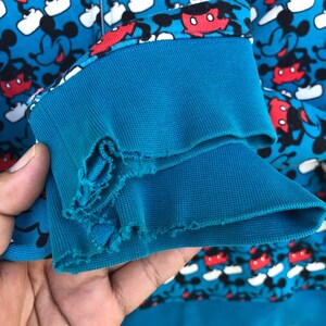 May include: A close-up of a blue sweatshirt sleeve with a Mickey Mouse pattern. The sleeve cuff is a darker blue and shows signs of wear. The background is filled with a repeating pattern of Mickey Mouse.