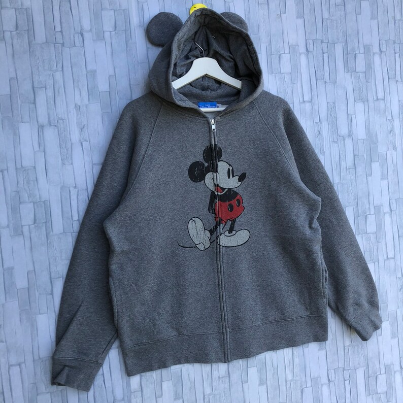 May include: A gray zip-up hoodie with a vintage Mickey Mouse graphic on the front. The hoodie has a hood with attached ears.