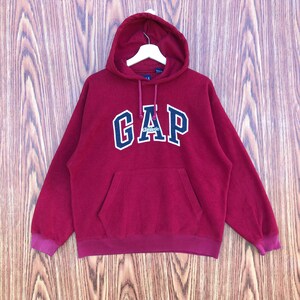 May include: A maroon GAP hoodie with a hood and a front pocket. The word "GAP" is printed across the chest in white with a blue outline. The word "Athletic" is printed below the word "GAP".