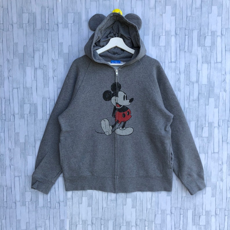 May include: A gray zip-up hoodie with a vintage Mickey Mouse graphic on the front. The hoodie has a hood with attached ears.