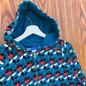 May include: A teal zip-up hoodie featuring a repeating pattern of Mickey Mouse. The design includes Mickey's face in red, black, and white. The hoodie has a teal hood lining and a white hanger.