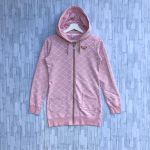 May include: A pink hooded sweatshirt with a white and brown pattern and a zipper closure. The sweatshirt has two pockets on the front and a small brown heart logo on the chest.