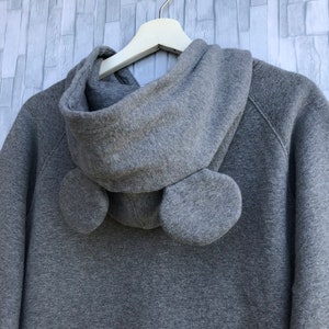 May include: Gray hooded sweatshirt with a large hood and two fabric ear-like details on the back.