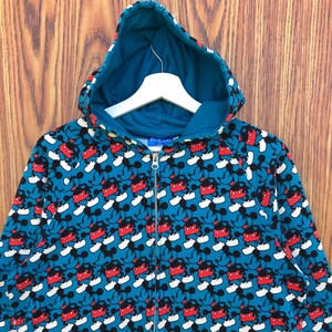 May include: A teal zip-up hoodie featuring a repeating pattern of Mickey Mouse. The design includes red, black, and white Mickey Mouse figures against a teal background. The hoodie has a teal-colored hood and a white hanger.