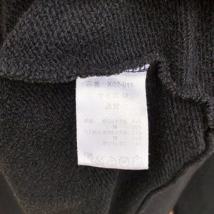 May include: Close-up of a dark gray fabric with a white tag. The tag has Japanese text and details the fabric composition: 63% polyester, 35% cotton, 63% polyester in the ribbing, 33% cotton, and 4% polyurethane.