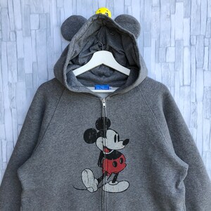 May include: Gray zip-up hoodie with a Mickey Mouse graphic on the front. The hoodie has a hood with attached ears.