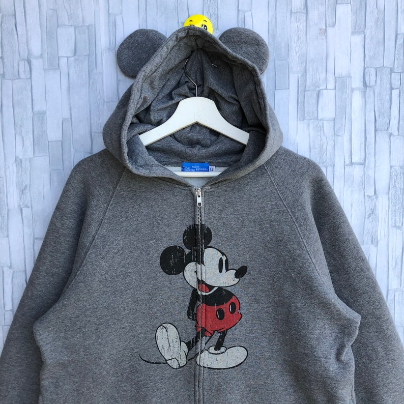 May include: Gray zip-up hoodie with a Mickey Mouse graphic on the front. The hoodie has a hood with attached ears.