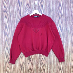 Può includere: Una felpa color amaranto con il nome del marchio "CHAPS" sul colletto. Presenta scollo e polsini a coste, dettagli trapuntati sulle spalle e un emblema triangolare sul petto con la scritta "ORIGINAL CHAPS DU BARON".