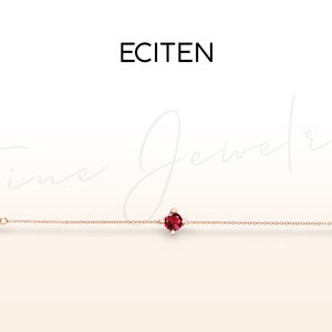 Könnte beinhalten: Ein zartes Armband aus Roségold mit einem einzigen roten Edelstein in der Mitte.