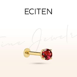 May include: Gold body jewelry with a red gemstone. ECITEN Fine Jewelry.