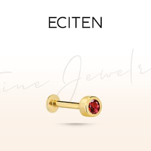 May include: Gold body jewelry with a small red gemstone. The jewelry is a barbell style with a flat back and a round front.