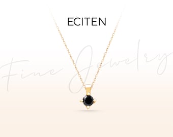 Op de afbeelding: Een gouden ketting met een kleine, vierkant geslepen zwarte edelsteen hanger. De ketting heeft een fijne ketting en de achtergrond is zacht en neutraal. Het woord "ECITEN" staat bovenaan.