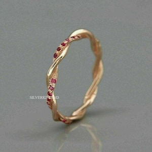 Op de afbeelding: Een goudkleurige ring met een gedraaid ontwerp. Kleine rode edelstenen zijn langs één kant van de ring gezet. De ring wordt getoond tegen een grijze achtergrond. De tekst "SILVERKINGND" is zichtbaar op de ring.