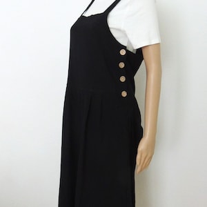 May include: Black jumpsuit with a white top underneath. The jumpsuit has a wide leg and features a row of buttons down the side.